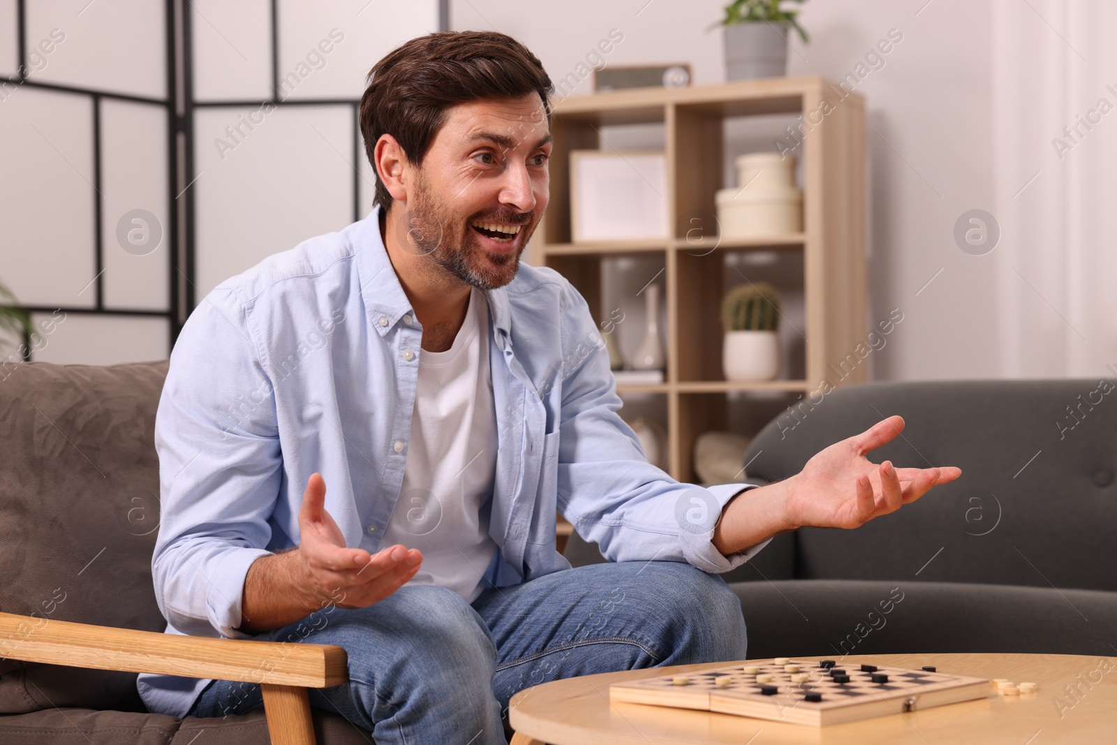 Photo of Emotional man playing checkers in armchair at home