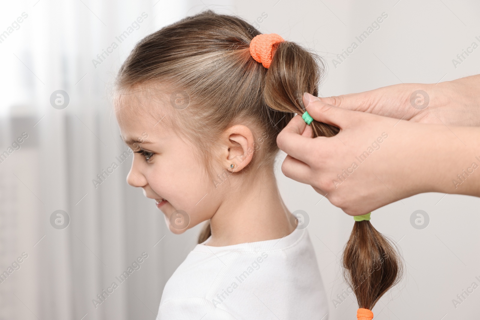 Photo of Professional stylist braiding girl's hair indoors, closeup