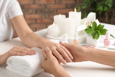 Cosmetologist massaging client's hand at table in spa salon, closeup