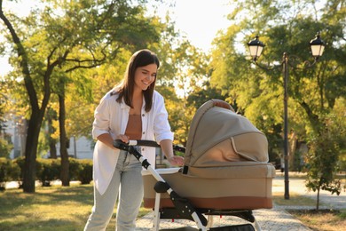 Photo of Young mother walking with her baby in stroller at park on sunny day