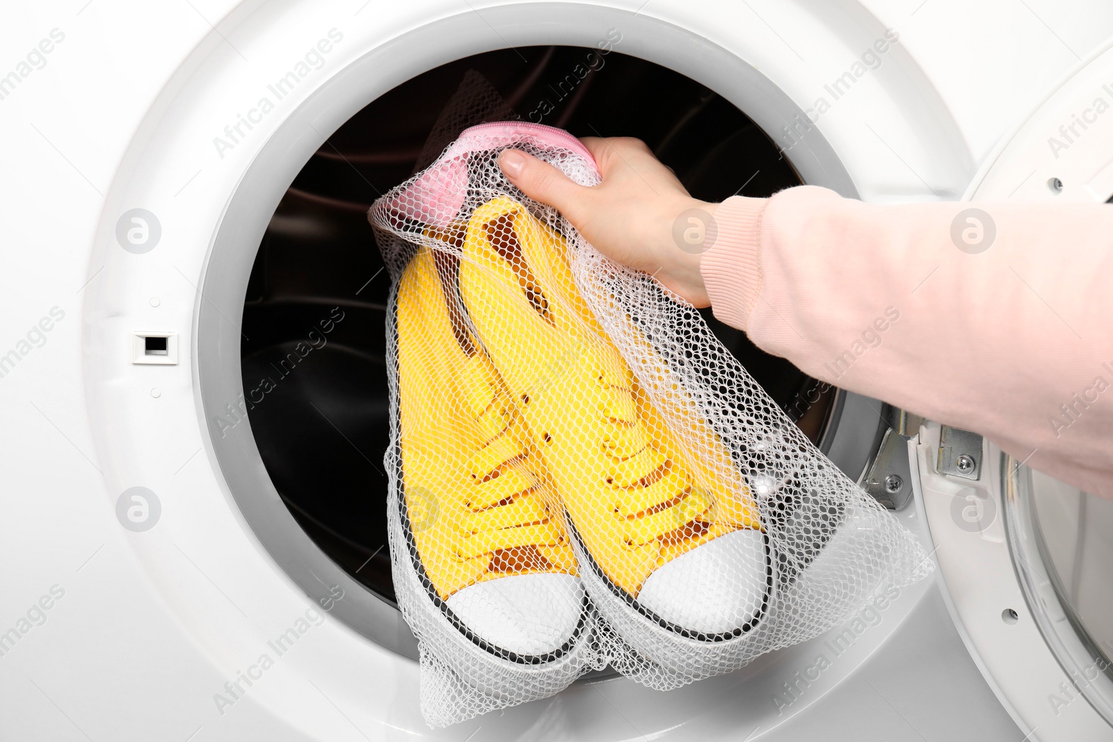 Photo of Woman putting stylish sneakers into washing machine, closeup