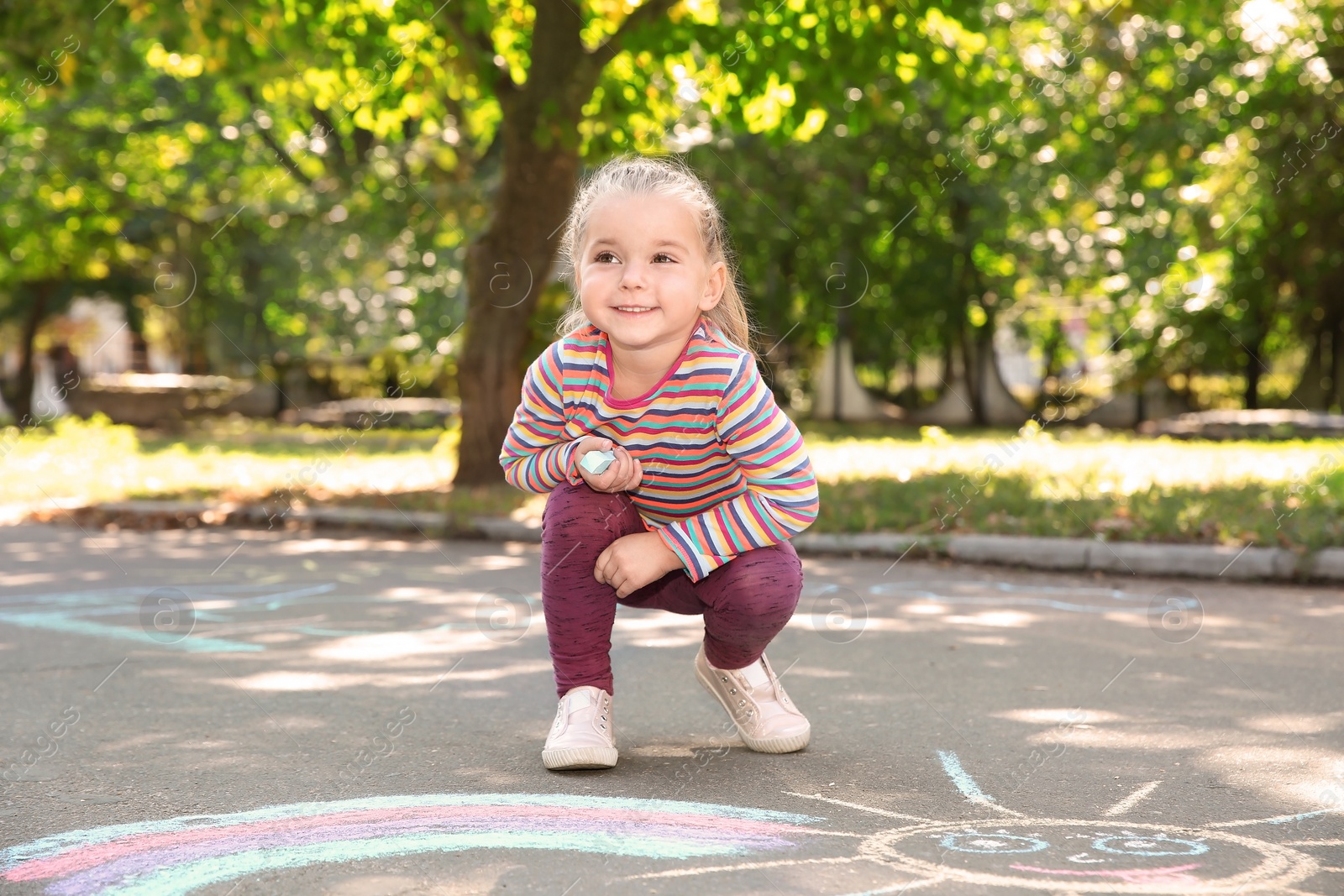 Photo of Little child drawing with colorful chalk on asphalt