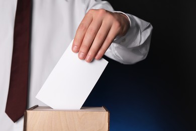 Man putting his vote into ballot box on dark blue background, closeup