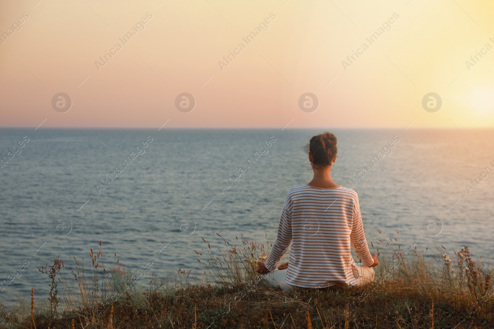 Photo of Woman meditating near sea, back view. Space for text