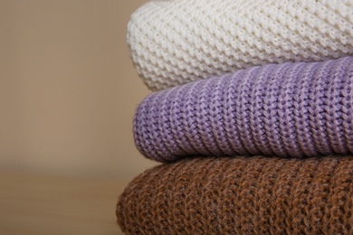 Stack of folded knitted sweaters on beige background, closeup