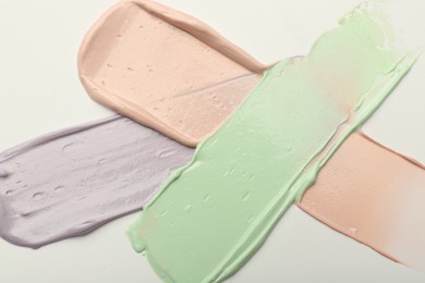 Photo of Strokes of pink, green and purple color correcting concealers on white background