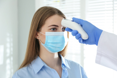 Doctor measuring patient's temperature with non contact infrared thermometer in office, closeup