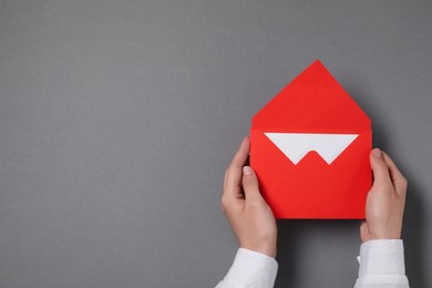 Woman holding letter envelope with card at grey table, top view. Space for text