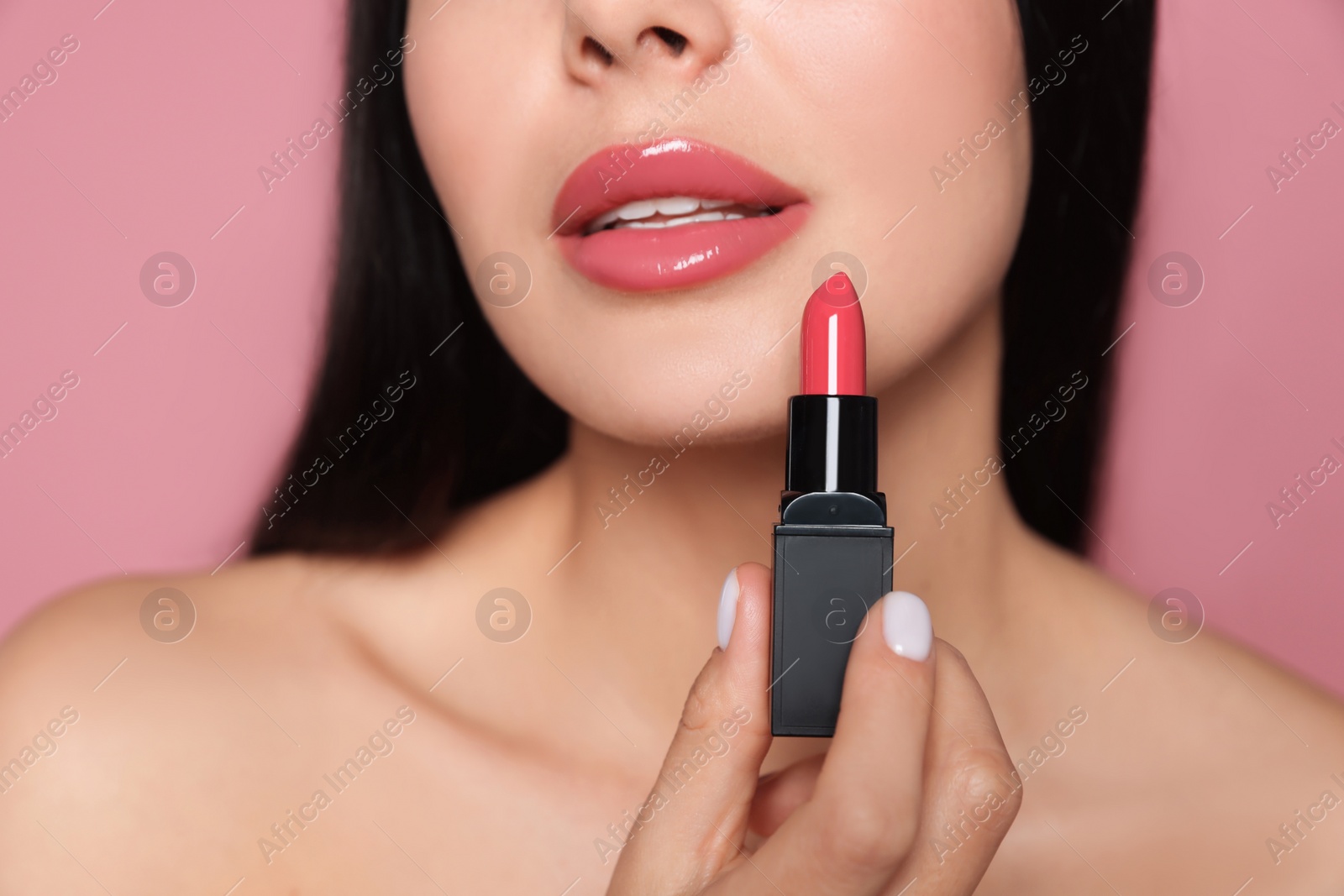 Photo of Young woman with beautiful makeup holding glossy lipstick on pink background, closeup