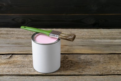 Photo of Can of pale pink paint with brush on wooden table. Space for text