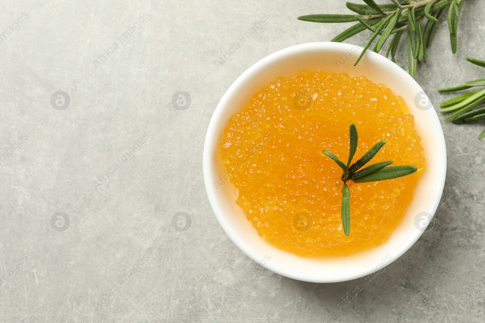 Photo of Fresh pike caviar in bowl and rosemary on light grey table, top view. Space for text