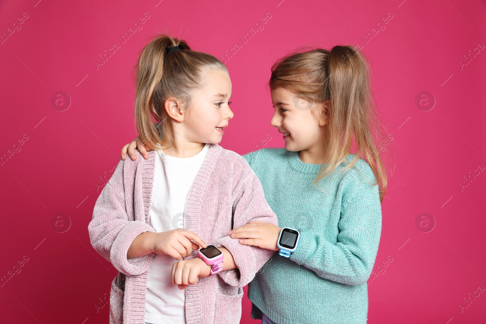 Photo of Little girls with smart watches on pink background