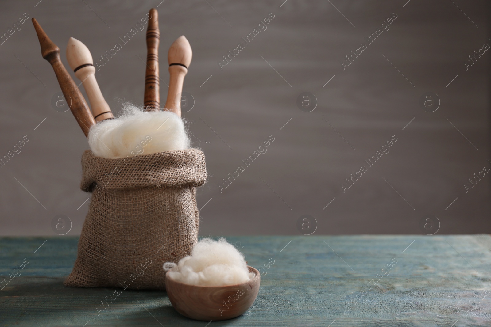 Photo of Soft white wool and spindles on blue wooden table. Space for text