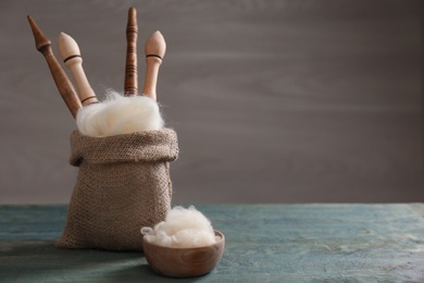 Soft white wool and spindles on blue wooden table. Space for text