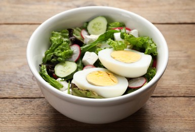 Photo of Delicious salad with boiled egg, feta cheese and vegetables on wooden table, closeup