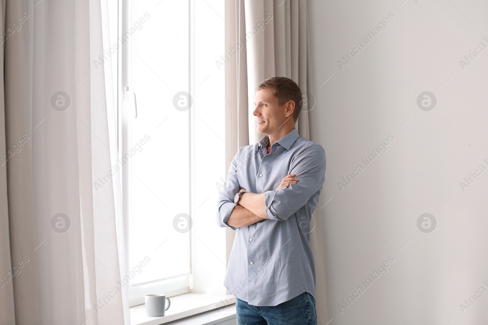 Photo of Mature man near window with open curtains at home. Space for text