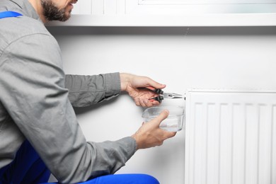 Photo of Professional plumber using pliers while preparing heating radiator for winter season, closeup