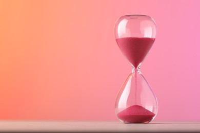 Photo of Hourglass with flowing pink sand on table against color background. Space for text