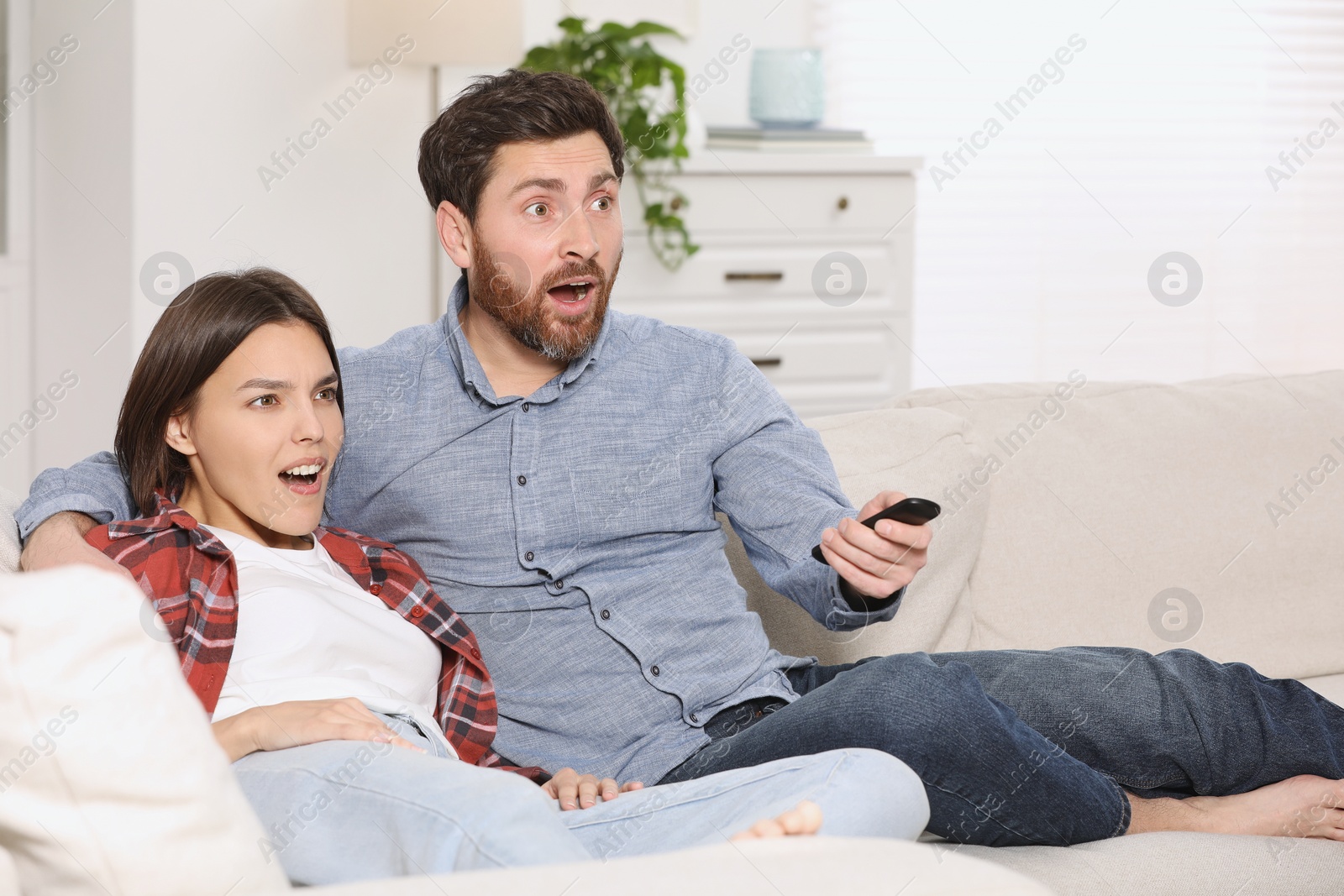 Photo of Surprised couple watching TV on sofa at home