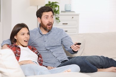 Surprised couple watching TV on sofa at home
