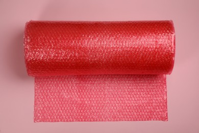 Photo of Bubble wrap roll on light pink background, top view