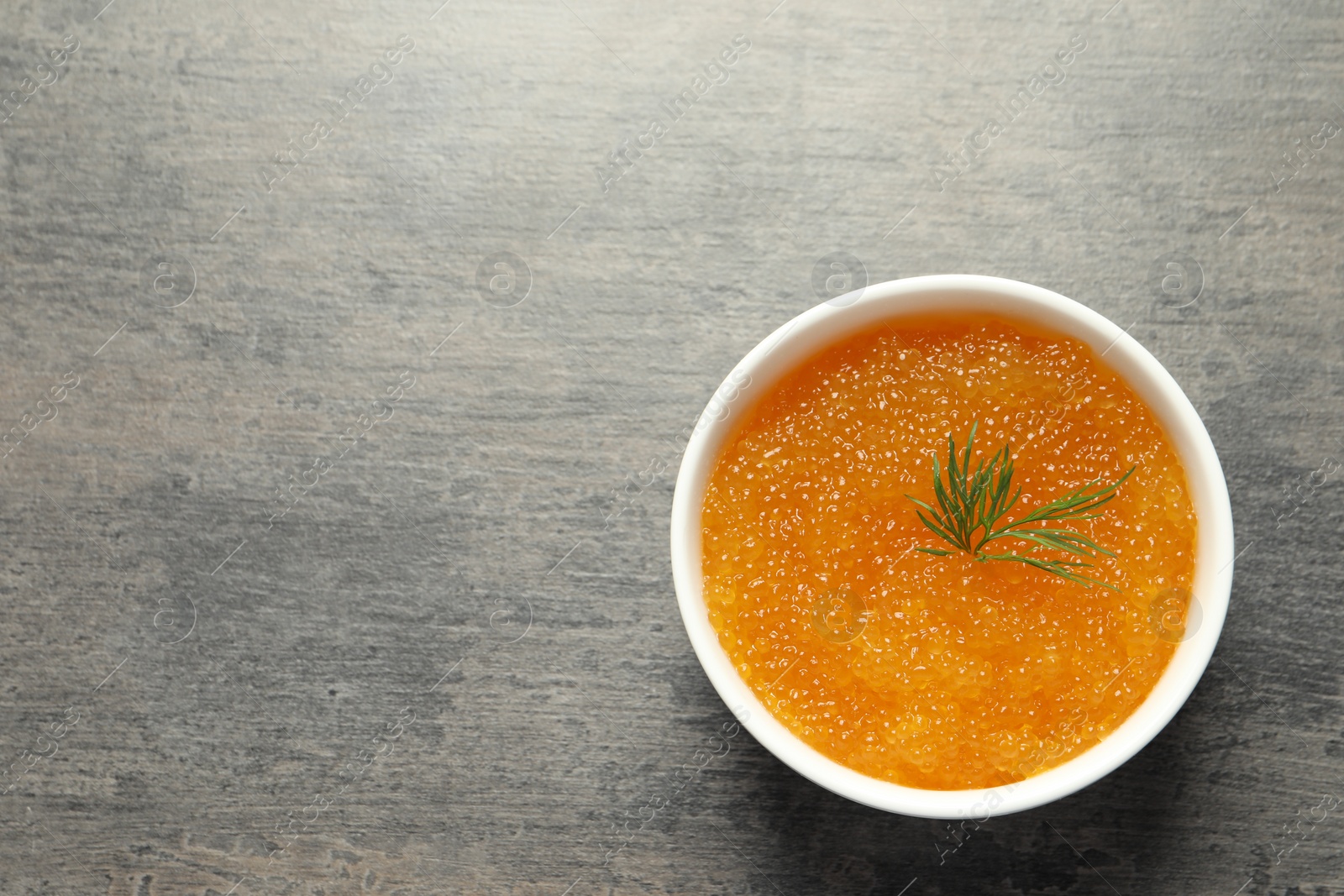 Photo of Fresh pike caviar and dill in bowl on grey table, top view. Space for text