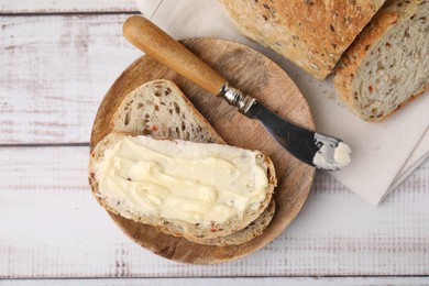 Tasty bread with butter and knife on white wooden table, flat lay