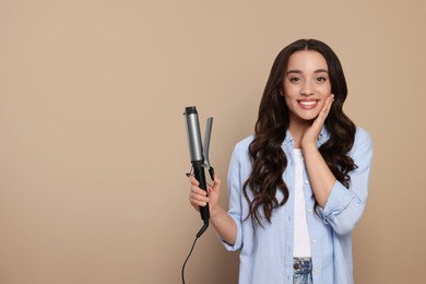 Happy woman with curling hair iron on beige background. Space for text