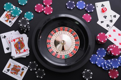 Photo of Roulette wheel, playing cards and chips on table, flat lay. Casino game