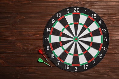 Dart board with color arrows on wooden background, top view. Space for text