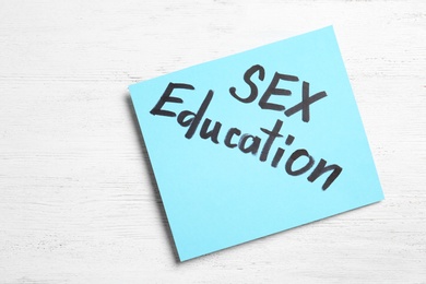 Note with phrase "SEX EDUCATION" on white wooden background, top view