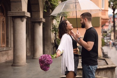 Young couple with umbrella enjoying time together under rain on city street, space for text