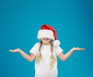 Cute little child wearing Santa hat on blue background. Christmas holiday