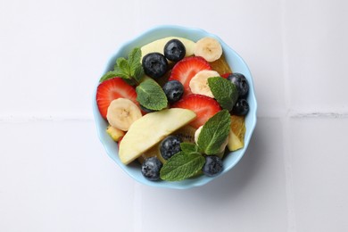 Photo of Tasty fruit salad in bowl on white tiled table, top view