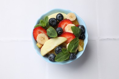 Tasty fruit salad in bowl on white tiled table, top view