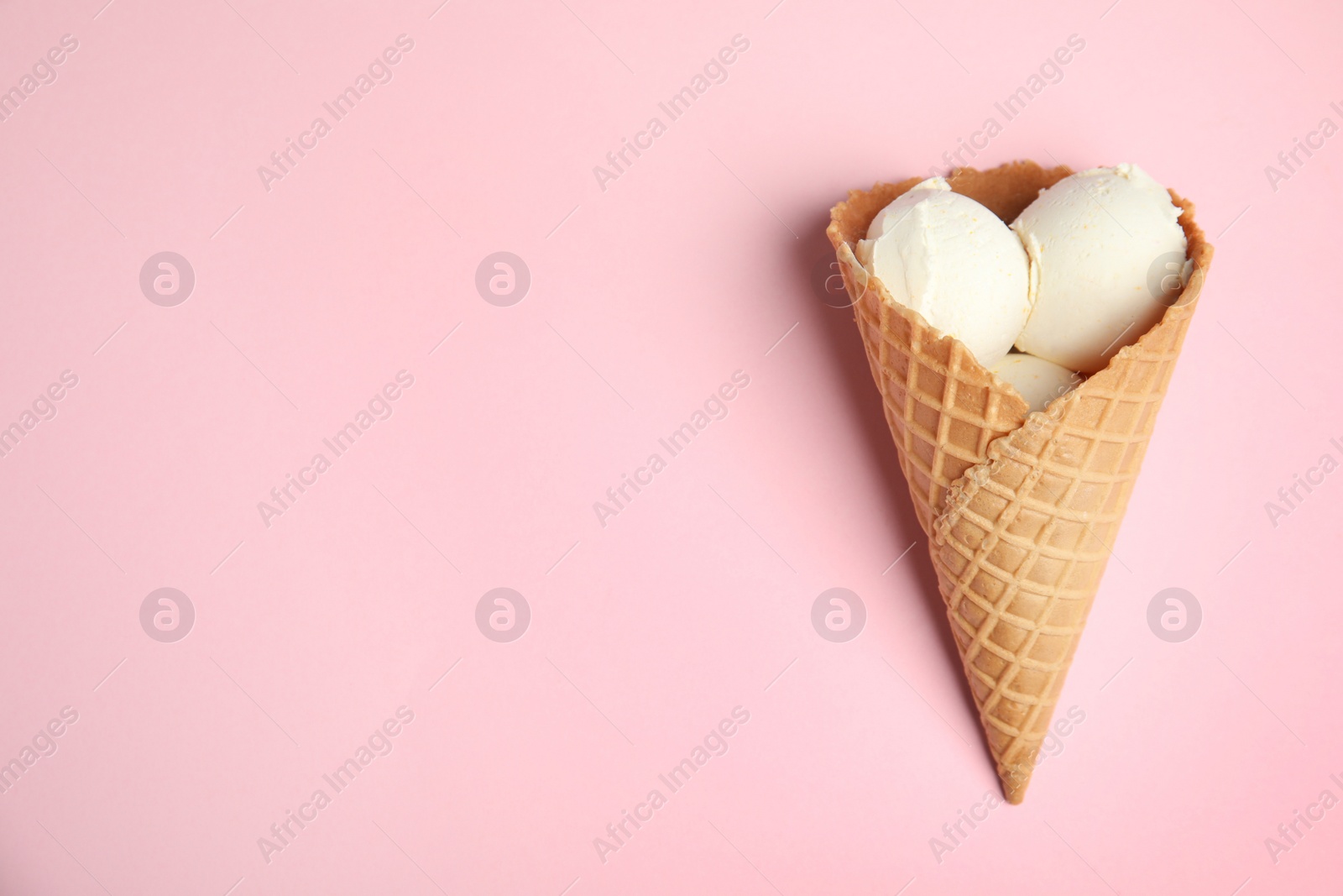 Photo of Delicious vanilla ice cream in wafer cone on pink background, top view. Space for text