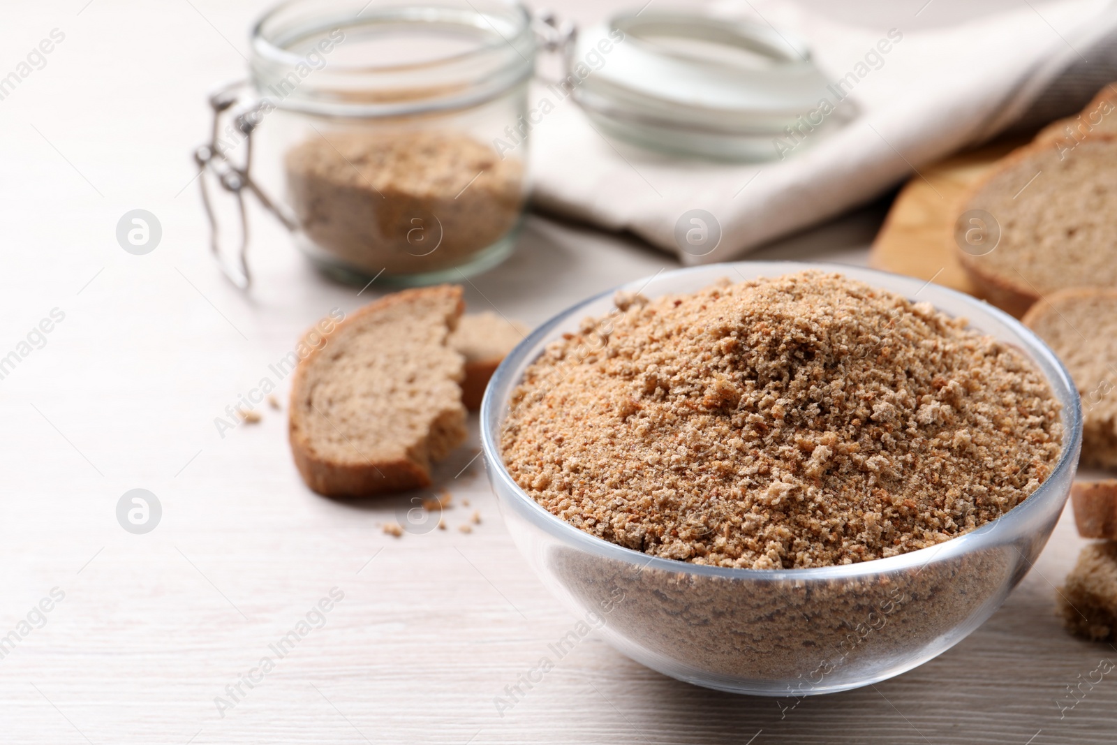 Photo of Fresh breadcrumbs in bowl on white wooden table. Space for text