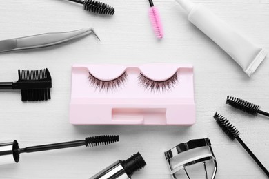 Flat lay composition with false eyelashes, brushes and tools on white wooden table