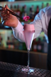 Photo of Bartender decorating fresh alcoholic cocktail with flower on bar counter, closeup