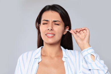 Young woman cleaning ear with cotton swab on light grey background