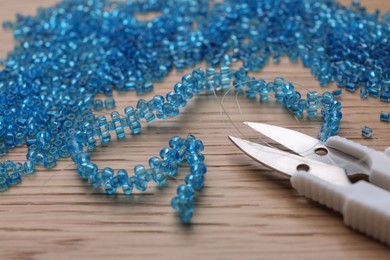 Photo of Bright light blue glass beads, bracelet and scissors on wooden table, closeup