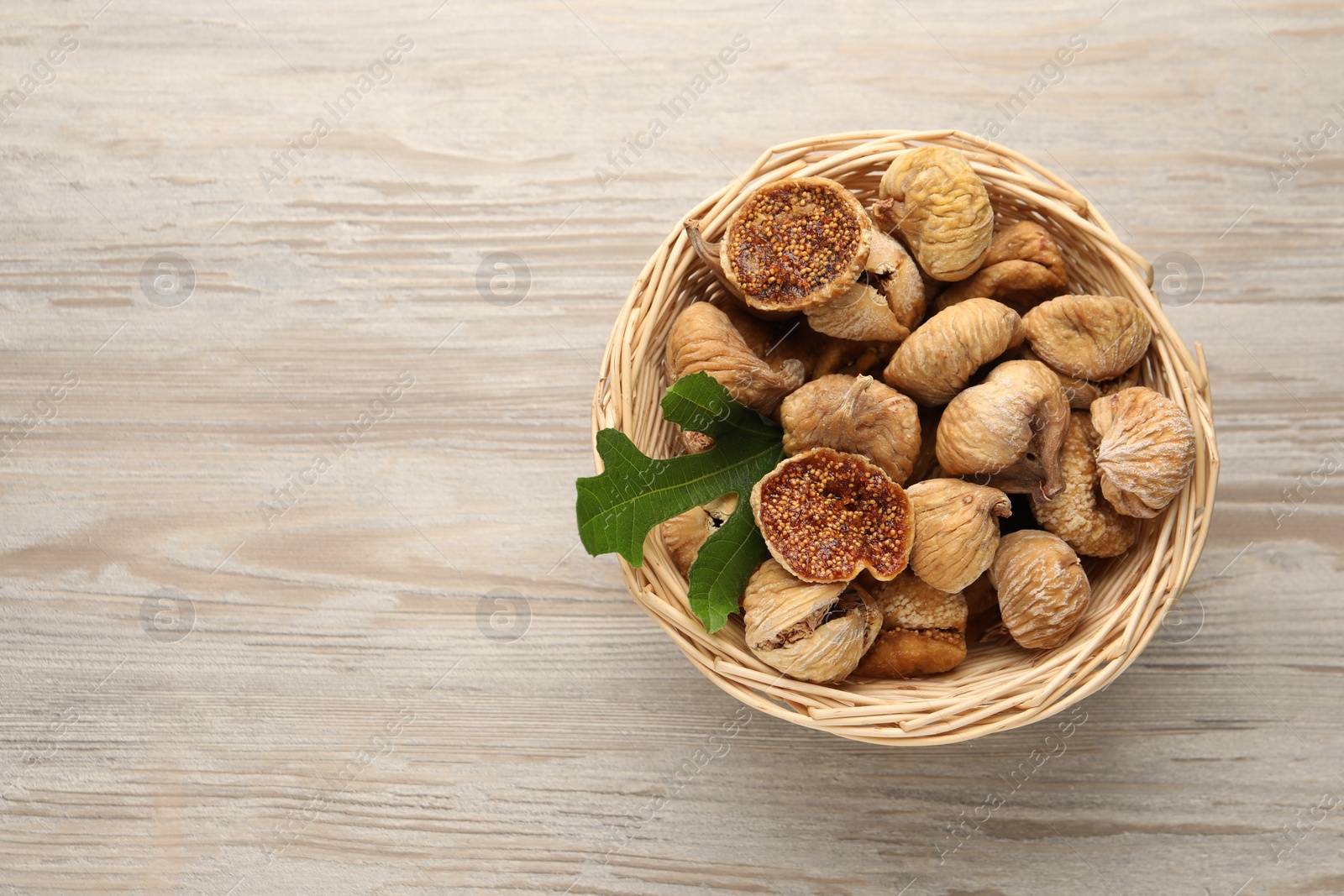 Photo of Wicker basket with tasty dried figs and green leaf on light wooden table, top view. Space for text