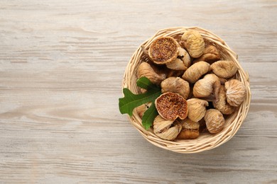 Photo of Wicker basket with tasty dried figs and green leaf on light wooden table, top view. Space for text