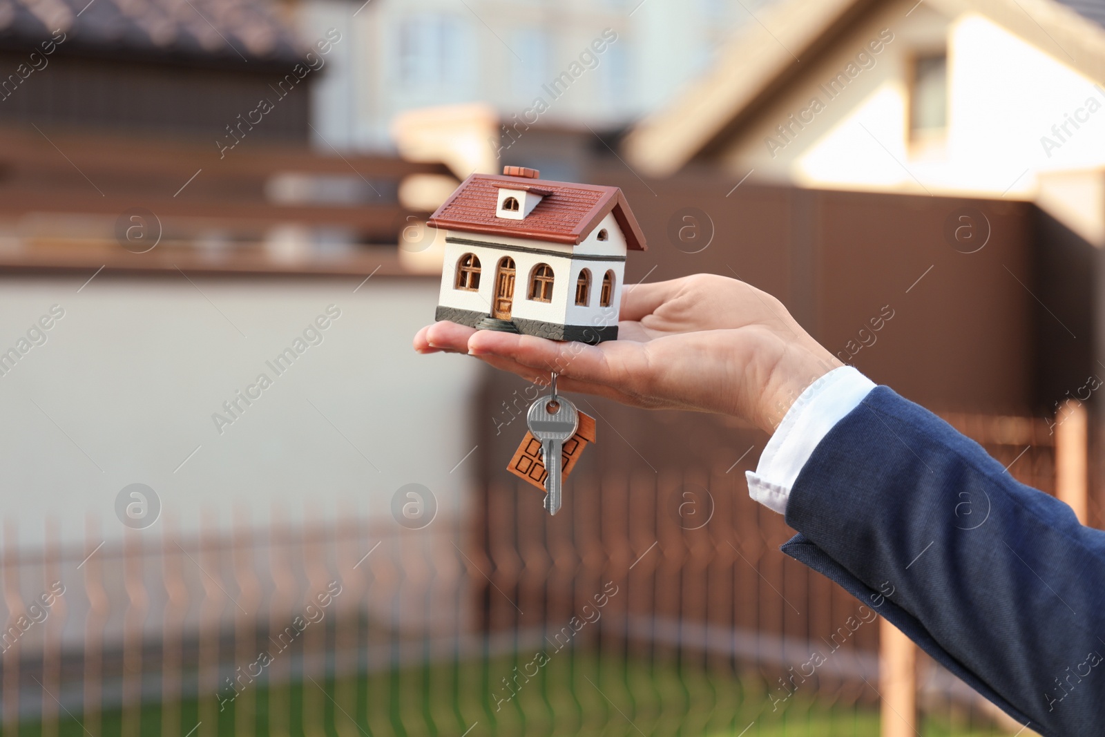 Photo of Real estate agent holding key and house model outdoors, closeup