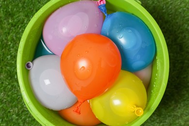 Bucket full of colorful water bombs on green grass, top view