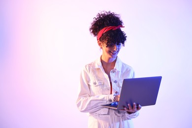 Photo of Beautiful young woman with laptop on color background in neon lights. Space for text