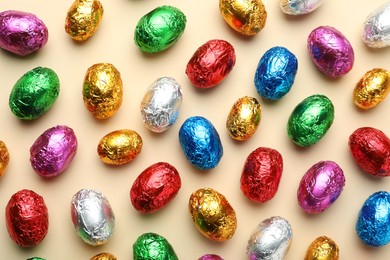 Photo of Chocolate eggs wrapped in colorful foil on beige background, flat lay