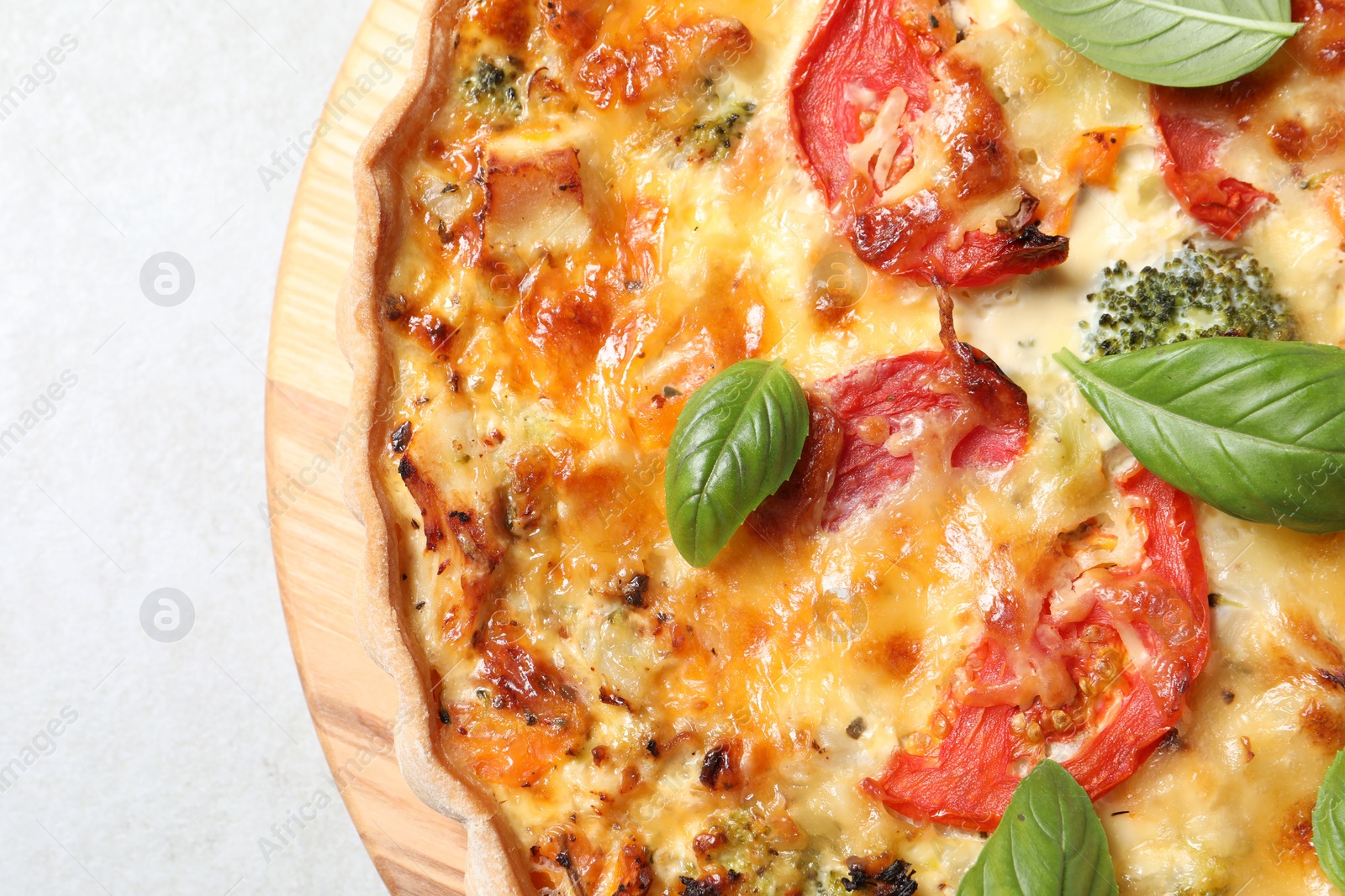 Photo of Tasty quiche with cheese, tomatoes and basil leaves on light grey table, top view