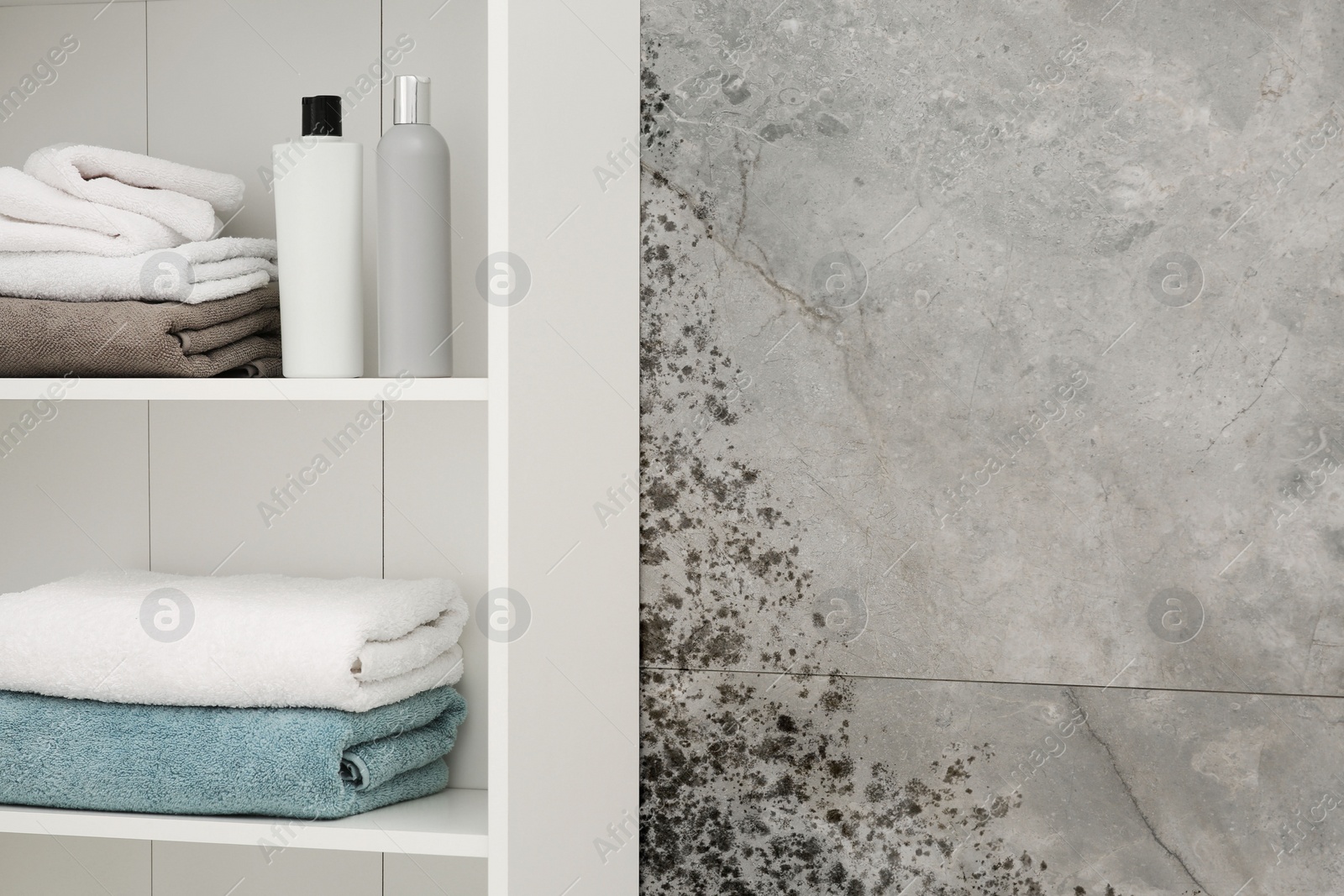 Image of Grey wall affected with mold. White rack with towels and personal care bottles in bathroom