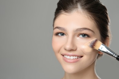 Photo of Beautiful girl applying foundation with brush against grey background. Space for text